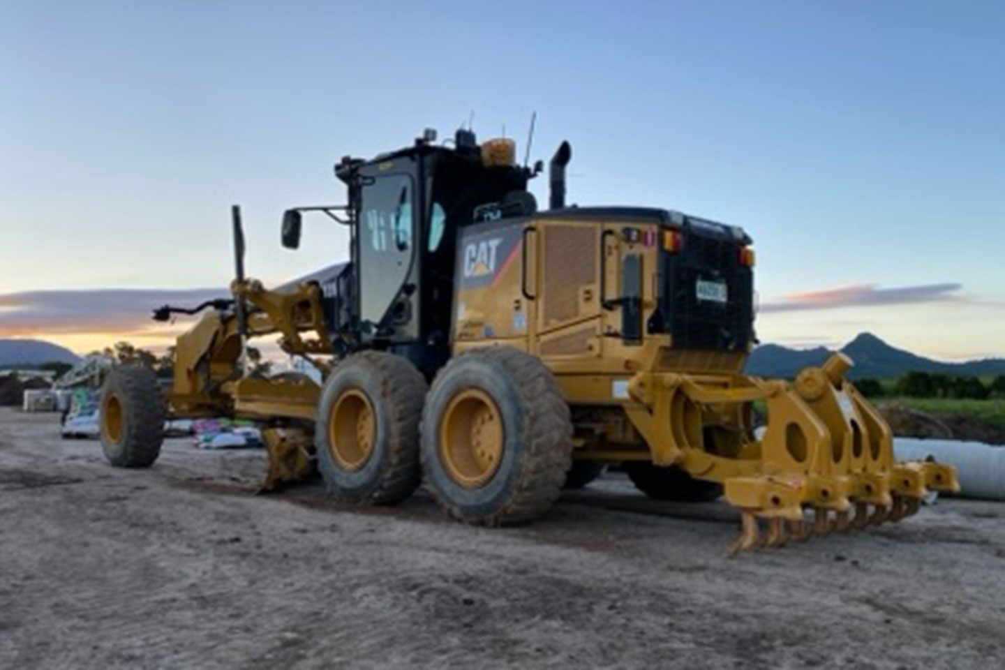 A grader on a dirt road with a blue sky background