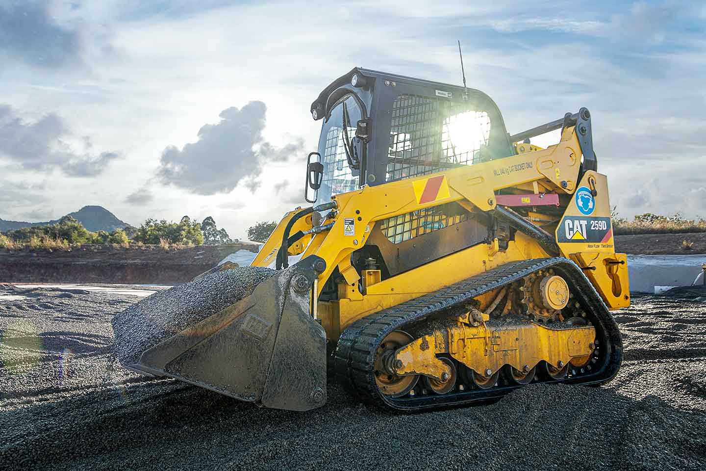 A skid steer on a gravel road with a cloudy sky background