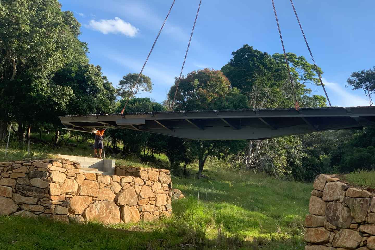Steel bridge span being lifted by crane chains into position between sandstone rock retaining walls